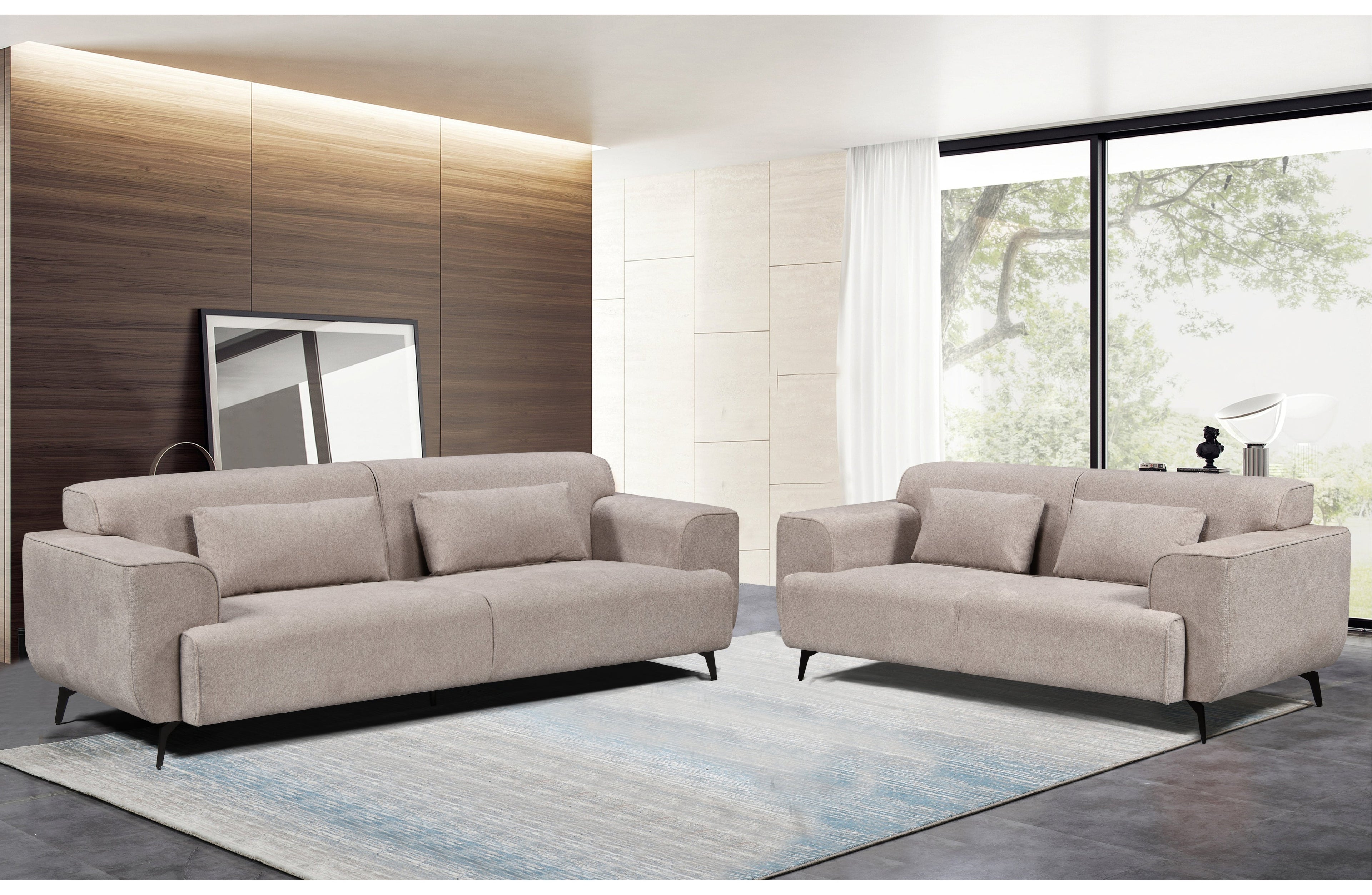Maddox Lounge Set in light grey, featuring a 3-seater and 2-seater fixed sofa with plush cushions and sleek black metal legs, styled in a modern living room with wood panel walls and large windows.