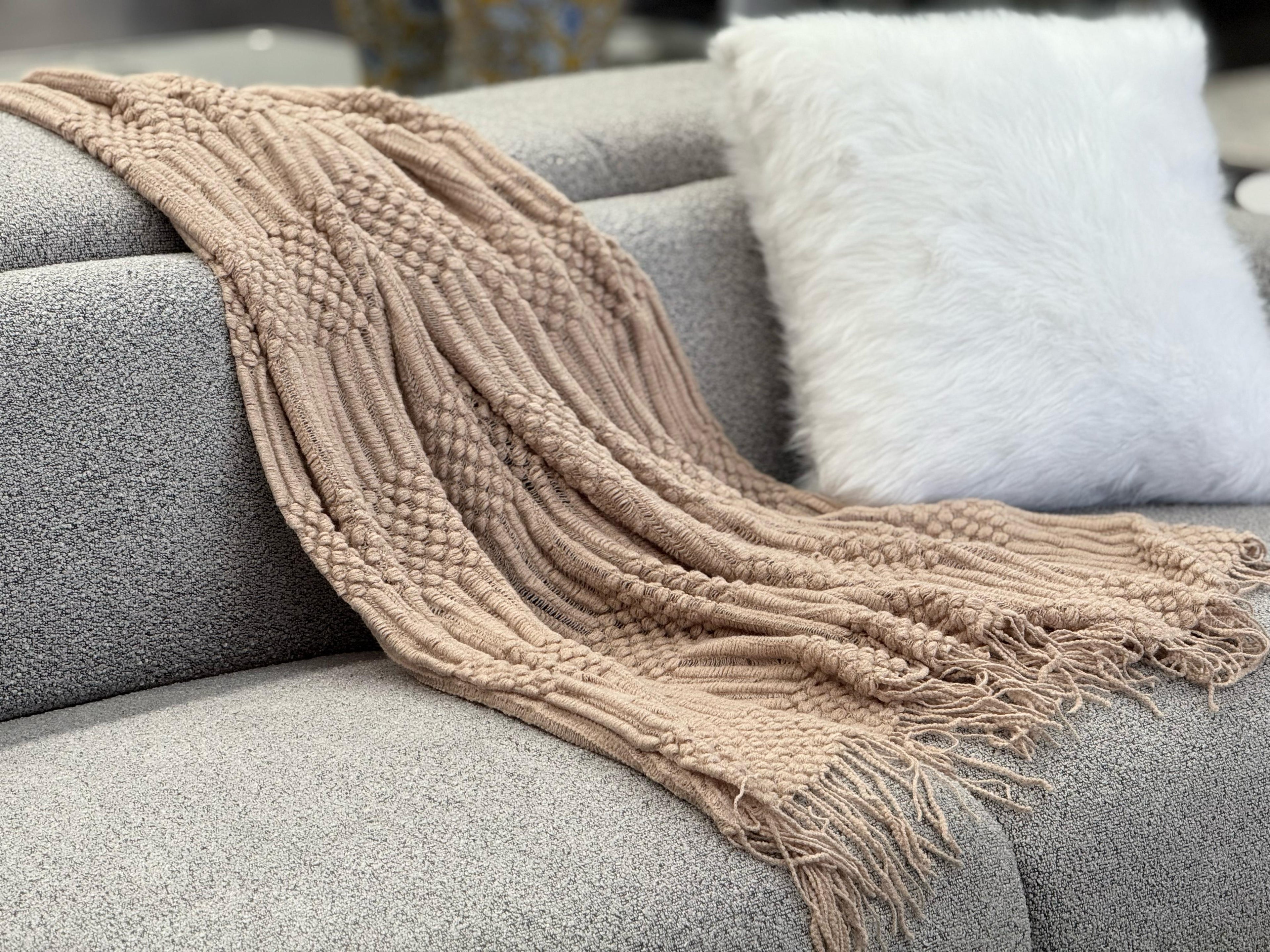Brown Tessa throw rug blanket draped over a cream sofa in a bright, modern living room.